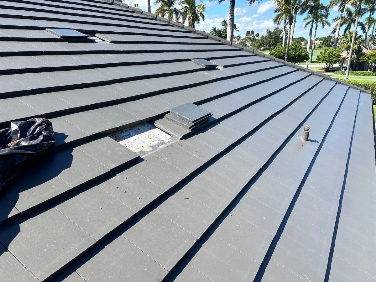 Opened section of a flat tile roof in Boca Raton showing the underlayment exposed with tiles stacked for re-use